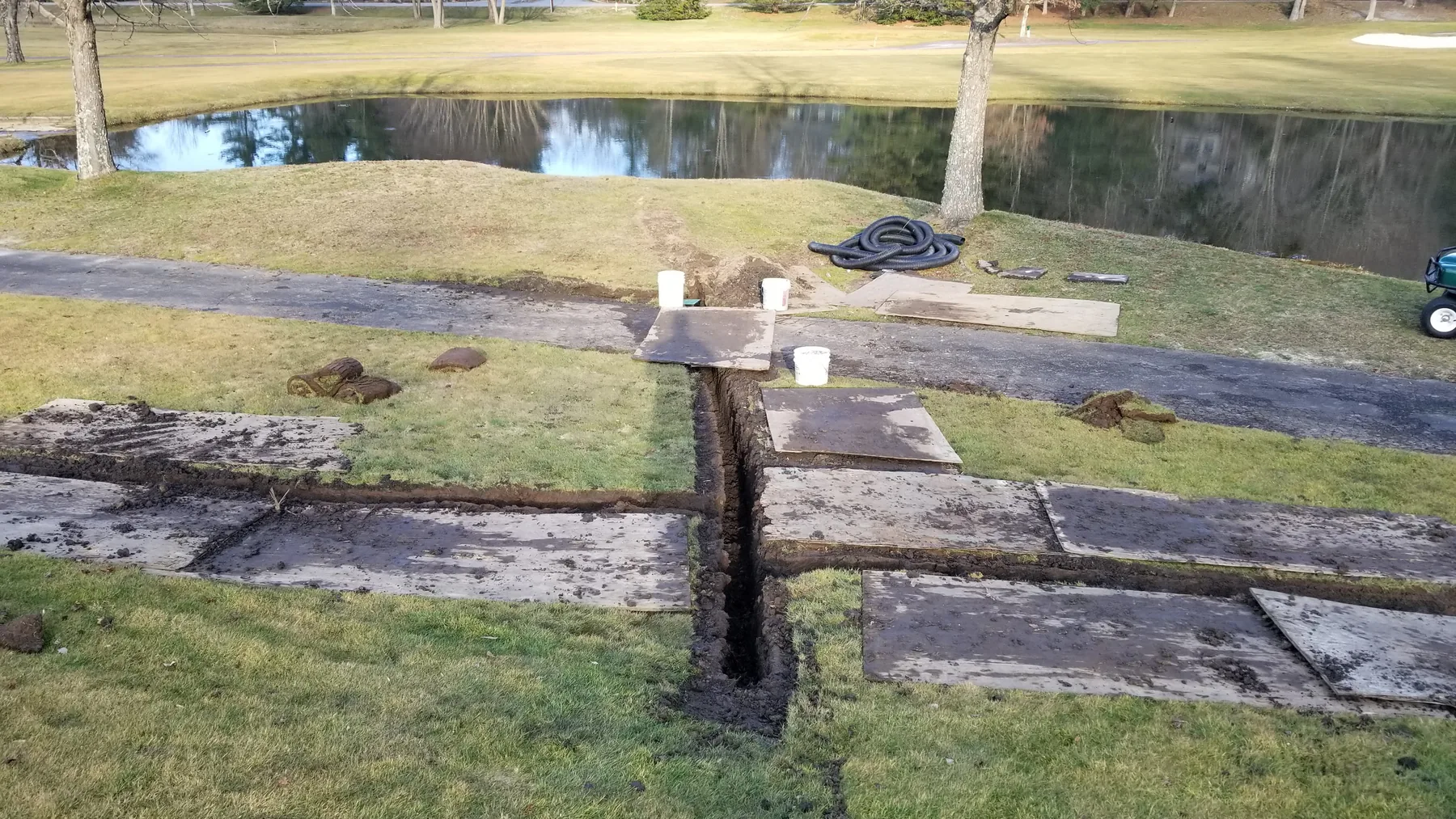 Drainage trench crossing a paved path near a pond