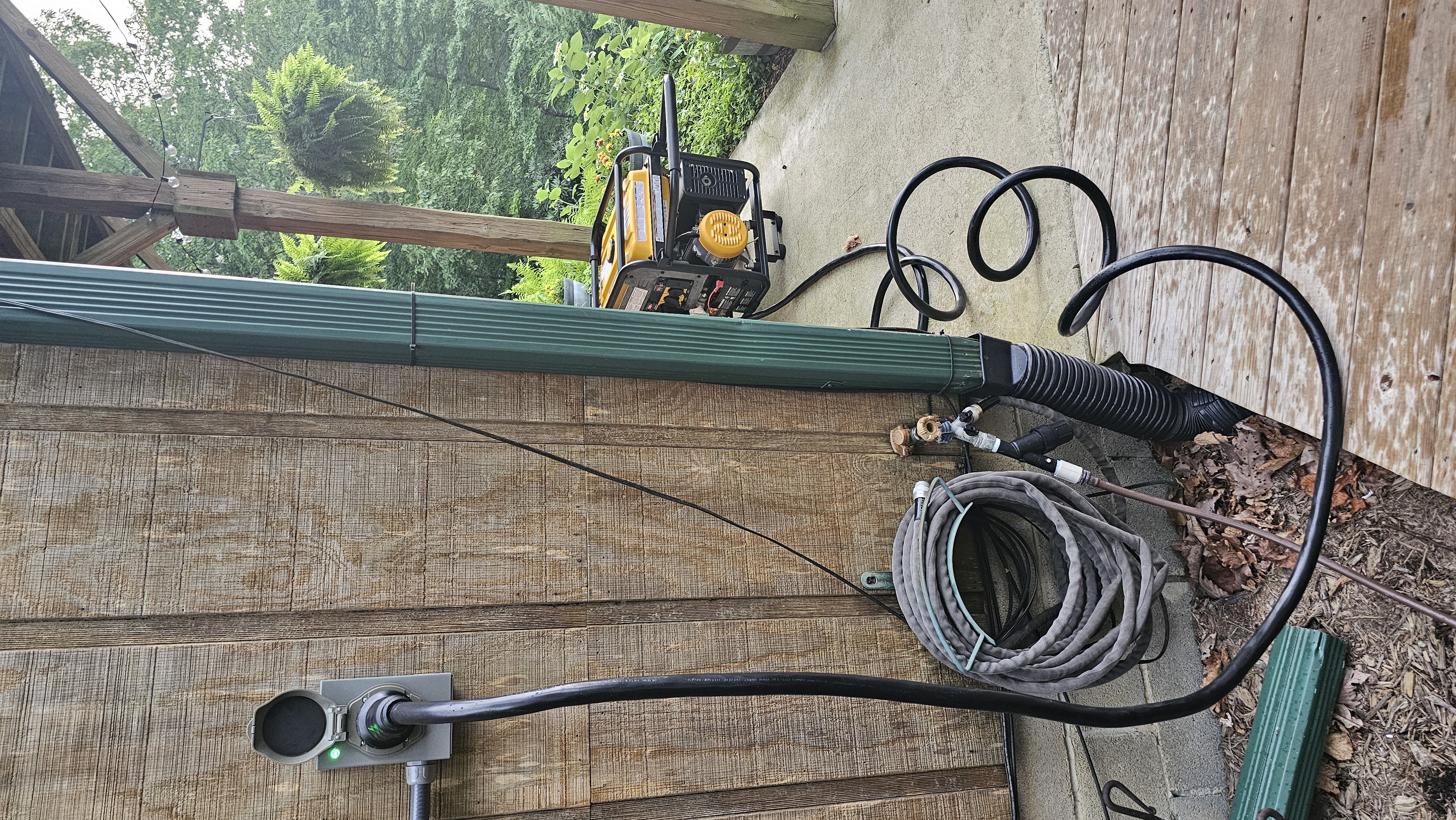 Portable generator connected to outdoor power inlet beside wooden wall.