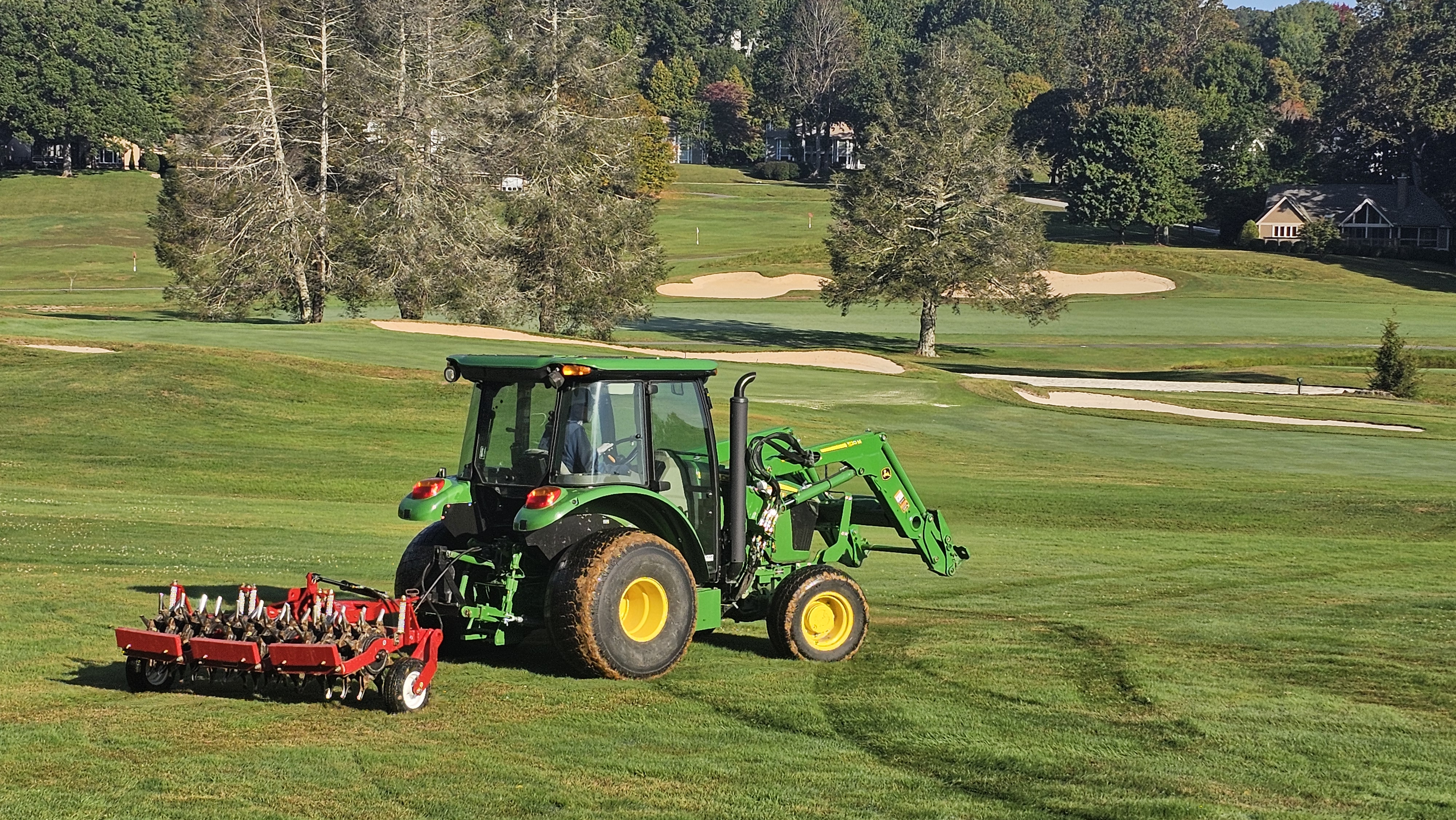 John Deere tractor aerating a fairway on a well-maintained golf course.
